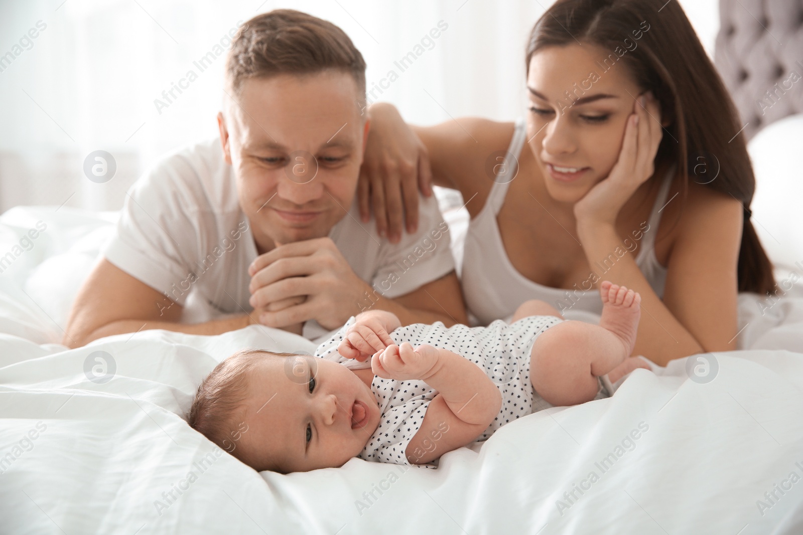 Photo of Happy couple with their newborn baby on bed