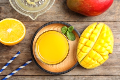 Photo of Glass of fresh mango drink and tropical fruits on wooden table, top view