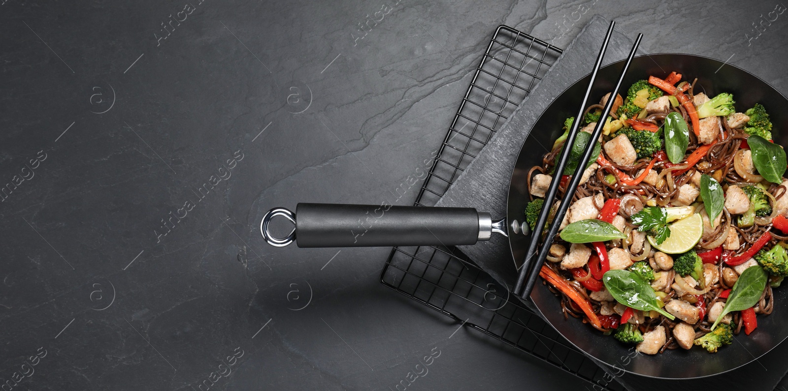 Photo of Stir-fry. Tasty noodles with meat in wok and chopsticks on grey textured table, top view. Space for text