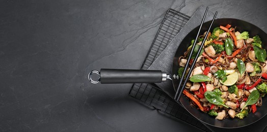 Photo of Stir-fry. Tasty noodles with meat in wok and chopsticks on grey textured table, top view. Space for text