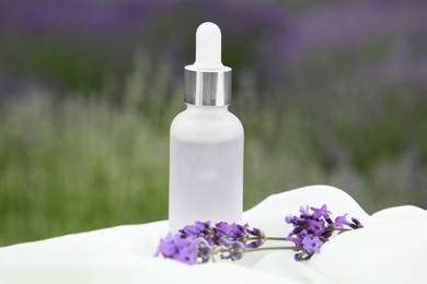 Photo of Essential oil and lavender flowers on table covered with white fabric in field