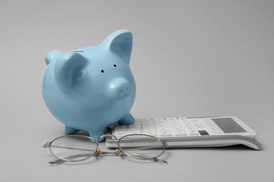 Calculator, glasses and piggy bank on grey background