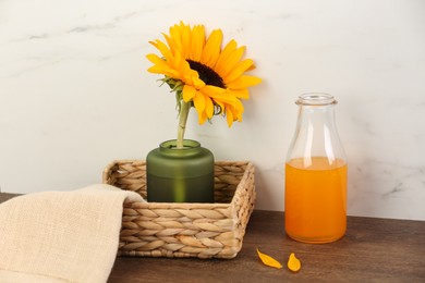 Photo of Vase with beautiful sunflower in wicker basket and bottle of orange juice on wooden table