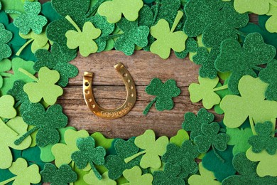 Photo of St. Patrick's day. Golden horseshoe and green decorative clover leaves on wooden table, flat lay