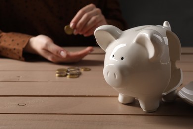Photo of Poverty. Woman counting coins at wooden table, focus on broken piggy bank