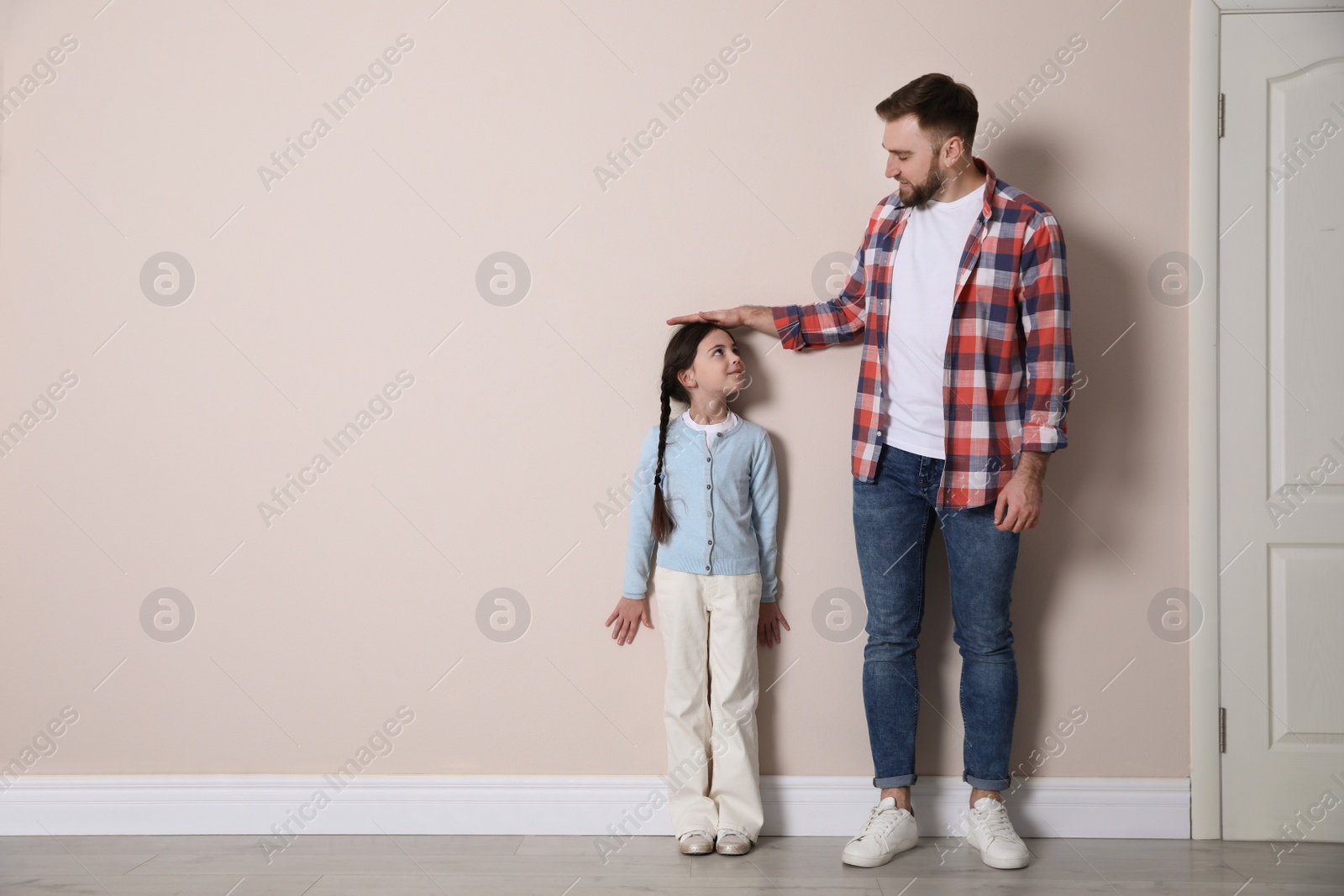 Photo of Father measuring daughter's height near beige wall indoors, space for text