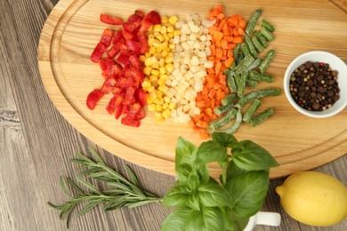 Photo of Mix of different frozen vegetables, spices and lemon on wooden table, flat lay