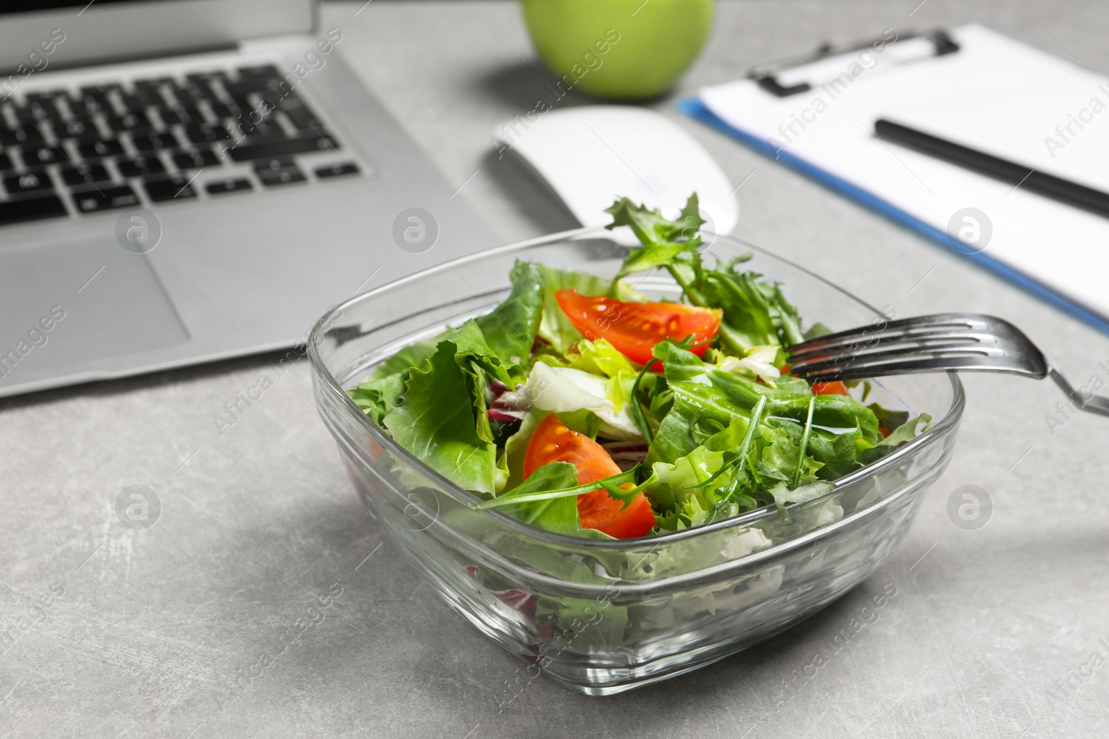 Photo of Fresh vegetable salad, laptop and fork on light grey table at workplace, closeup. Business lunch