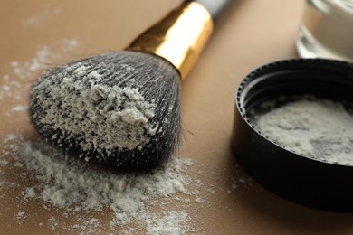 Makeup brush and lid with rice loose face powder on brown background, closeup