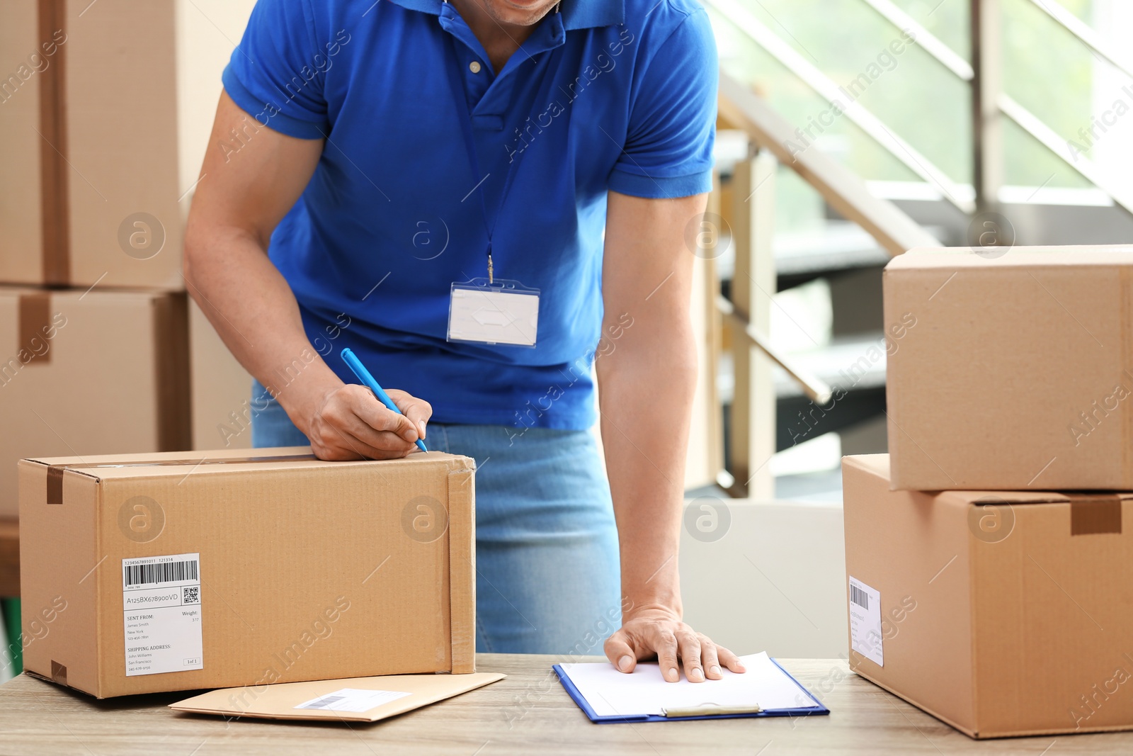 Photo of Young courier making notes on parcels at delivery department