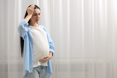 Pregnant woman suffering from headache indoors, space for text
