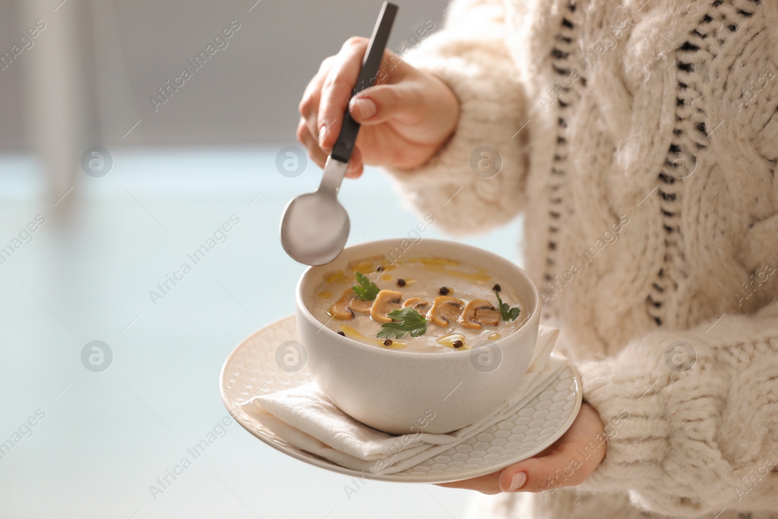 Photo of Young woman with bowl of cream soup on blurred background, closeup