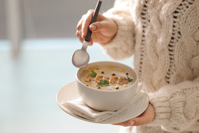 Photo of Young woman with bowl of cream soup on blurred background, closeup