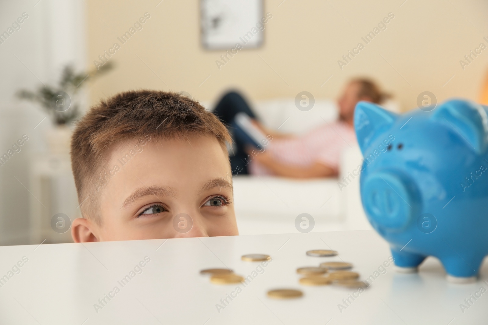 Photo of Curious boy near table with piggy bank and coins indoors