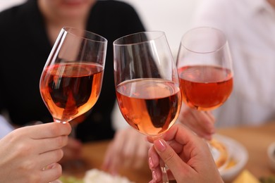 Photo of People clinking glasses with rose wine indoors, closeup