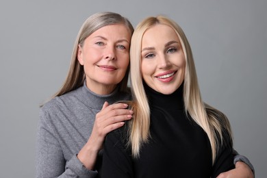 Family portrait of young woman and her mother on grey background