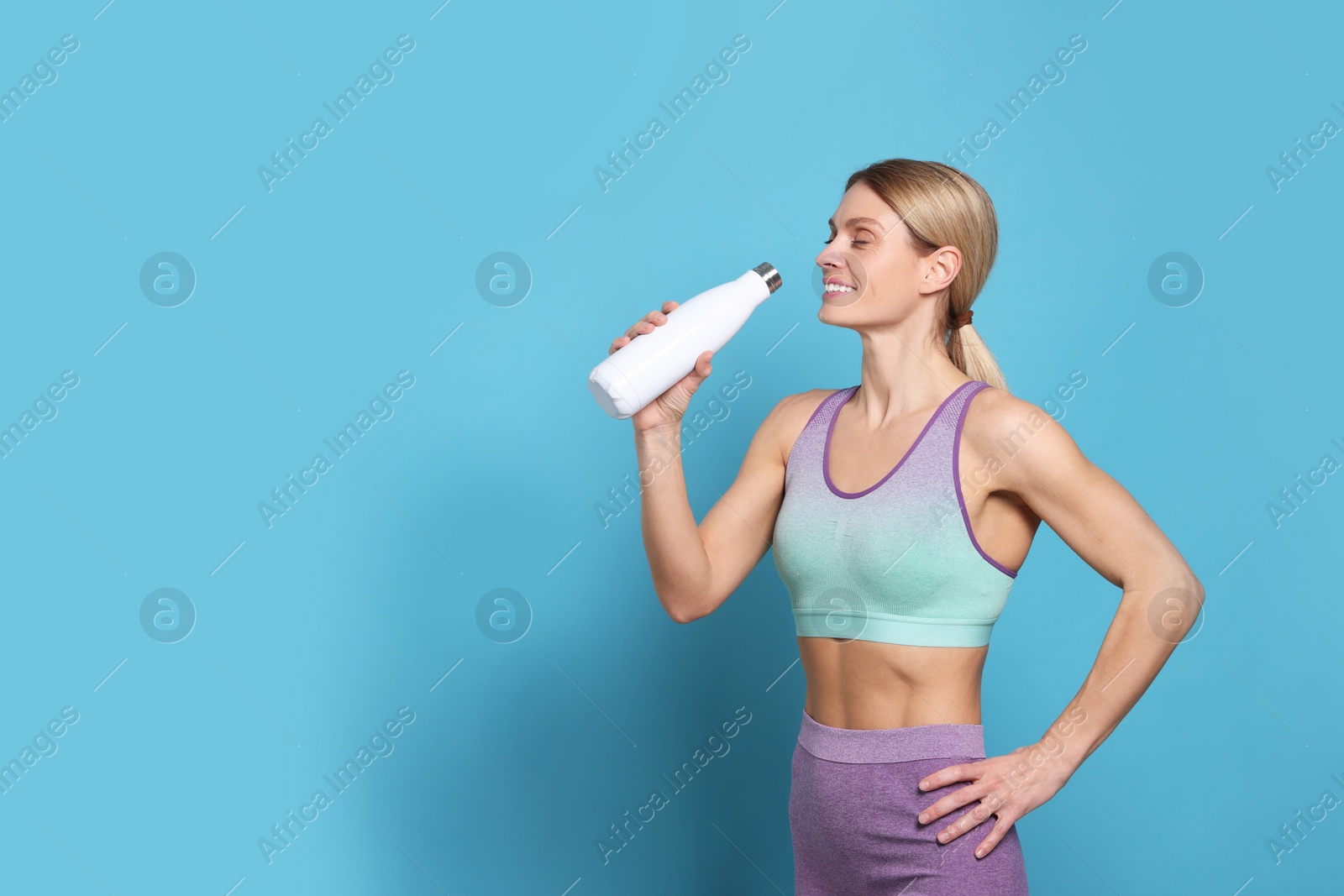 Photo of Sportswoman with thermo bottle on light blue background, space for text