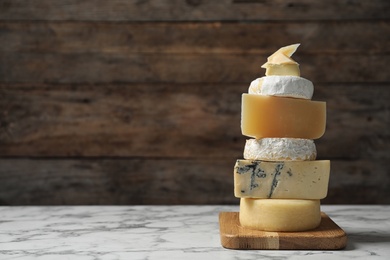 Photo of Different types of delicious cheese on marble table against wooden background, space for text