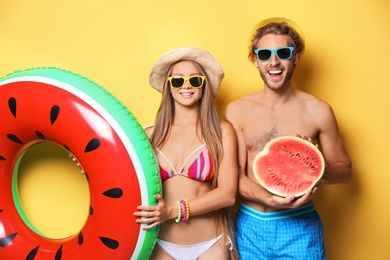 Photo of Young couple in beachwear with inflatable ring and watermelon on color background