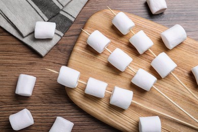 Photo of Sticks with delicious puffy marshmallows on wooden table, flat lay