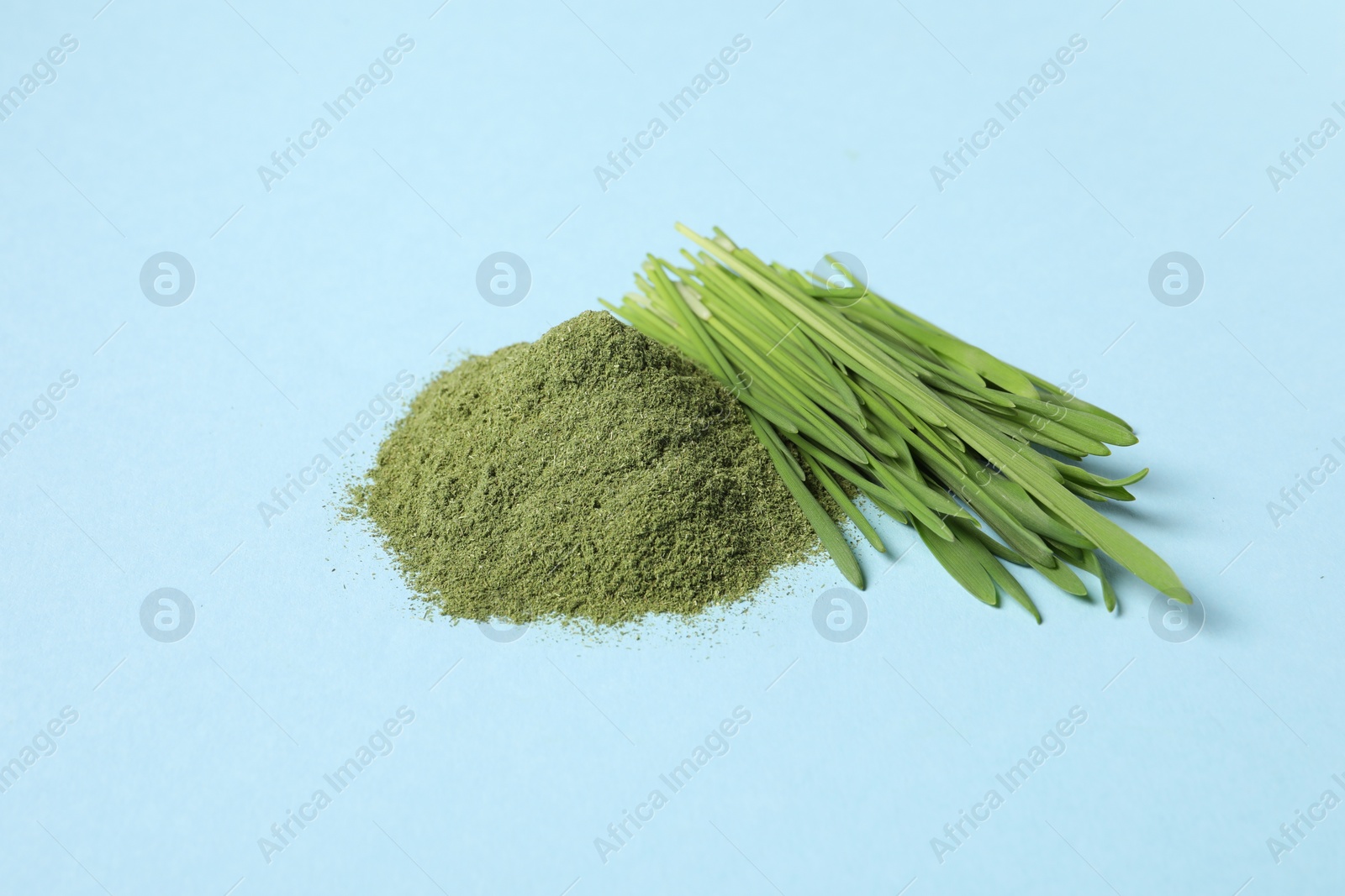 Photo of Pile of wheat grass powder and fresh sprouts on light blue table