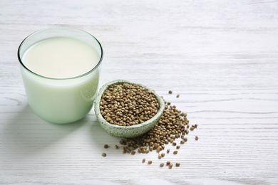 Photo of Bowl with hemp seeds and glass of milk on wooden background