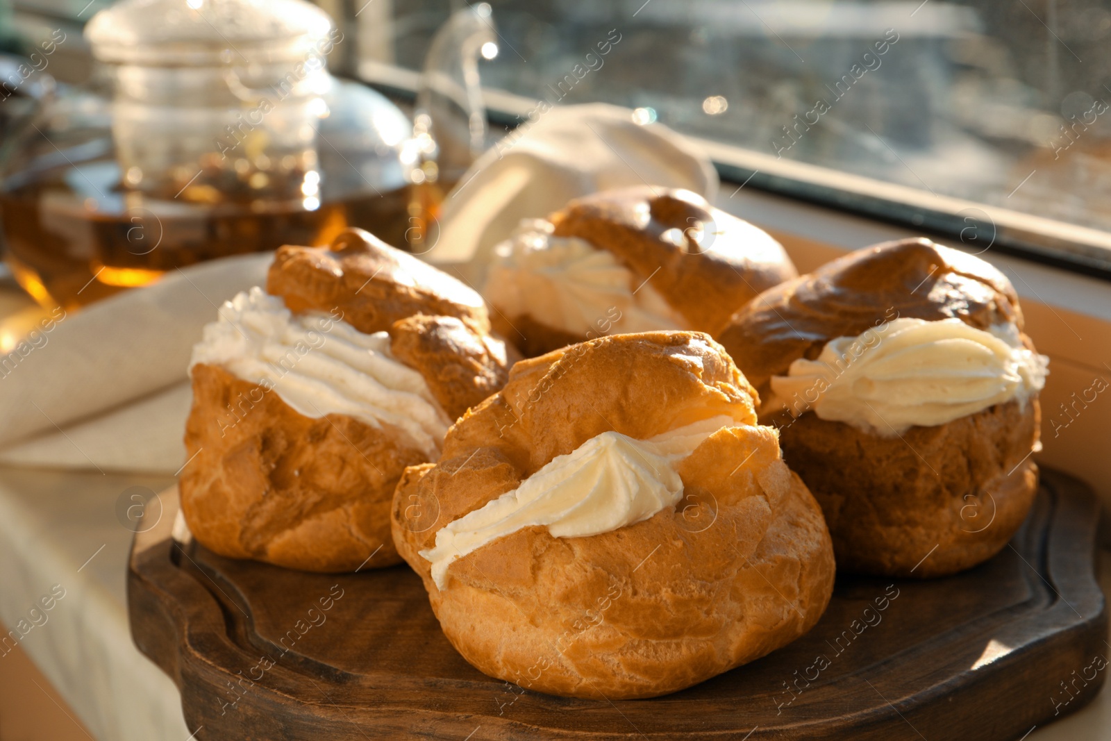 Photo of Delicious profiteroles filled with cream on window sill indoors, closeup