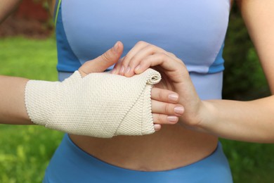 Woman wrapping hand in medical bandage outdoors, closeup