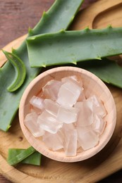 Photo of Aloe vera gel and slices of plant on wooden table, flat lay