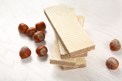 Photo of Delicious wafers with hazelnuts on white wooden background