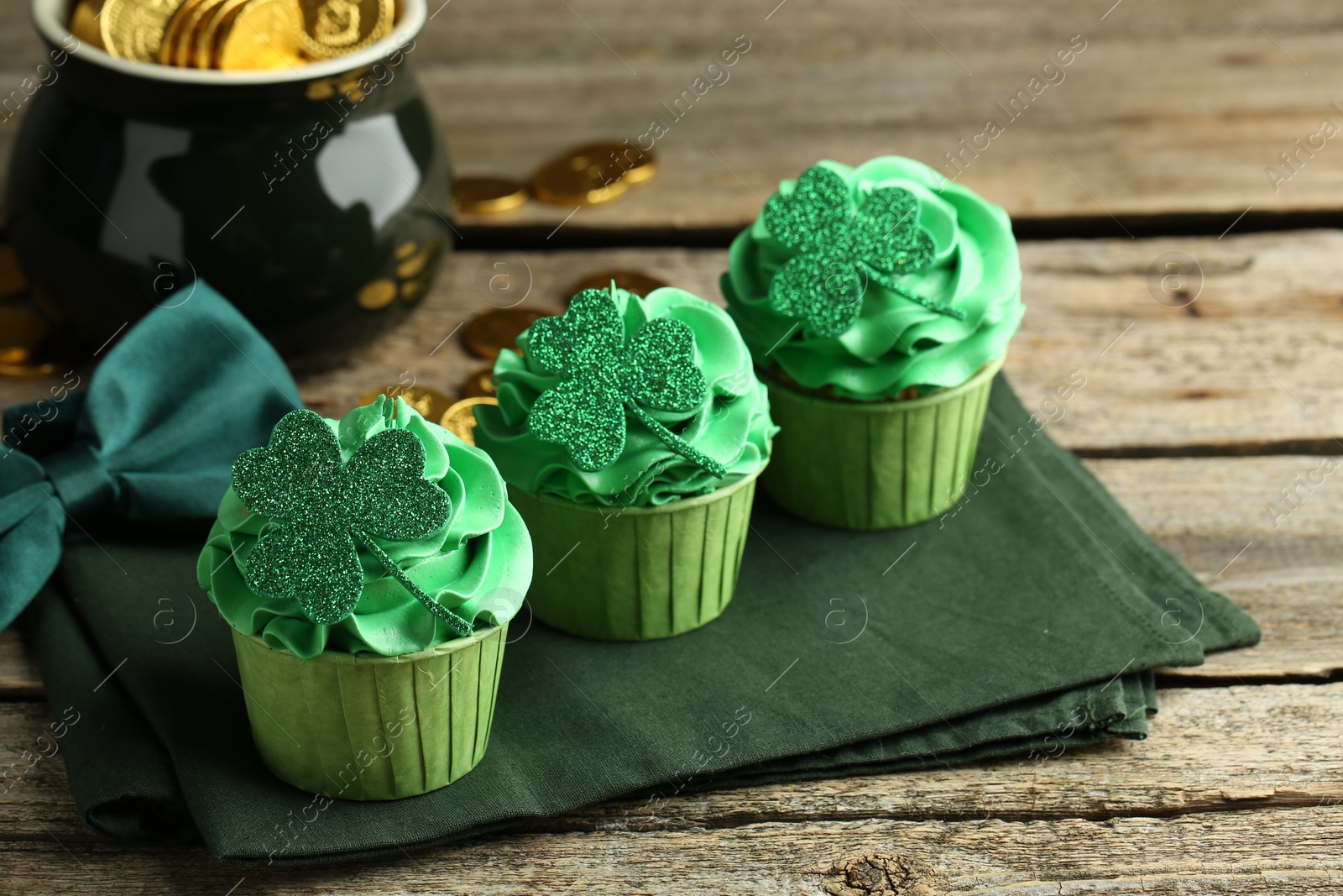 Photo of St. Patrick's day party. Tasty cupcakes with clover leaf toppers and green cream on wooden table, closeup