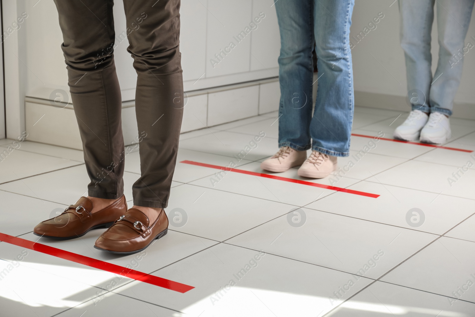 Photo of People standing in line behind taped floor markings for social distance indoors, closeup. Coronavirus pandemic