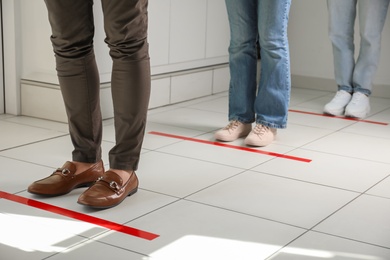 Photo of People standing in line behind taped floor markings for social distance indoors, closeup. Coronavirus pandemic