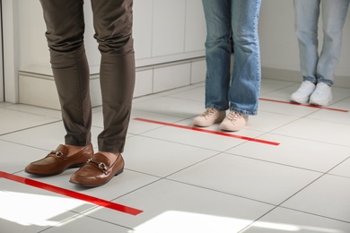 People standing in line behind taped floor markings for social distance indoors, closeup. Coronavirus pandemic