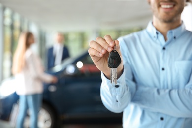 Photo of Salesman with car keys in modern auto dealership, closeup