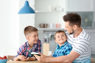 Photo of Dad and his sons reading interesting book in kitchen