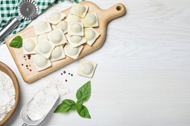 Photo of Uncooked ravioli, basil and peppercorns on white wooden table, flat lay. Space for text