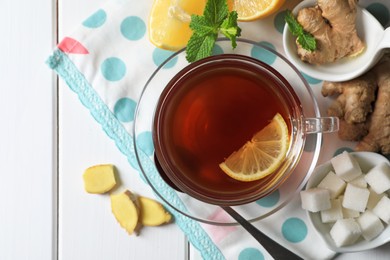 Cup of delicious ginger tea, sugar cubes and lemons on white wooden table, flat lay