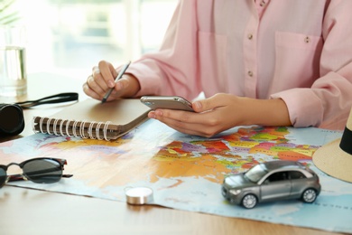 Photo of Woman with world map and smartphone planning trip at wooden table, closeup