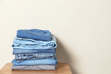 Photo of Stack of different jeans on table against light background. Space for text