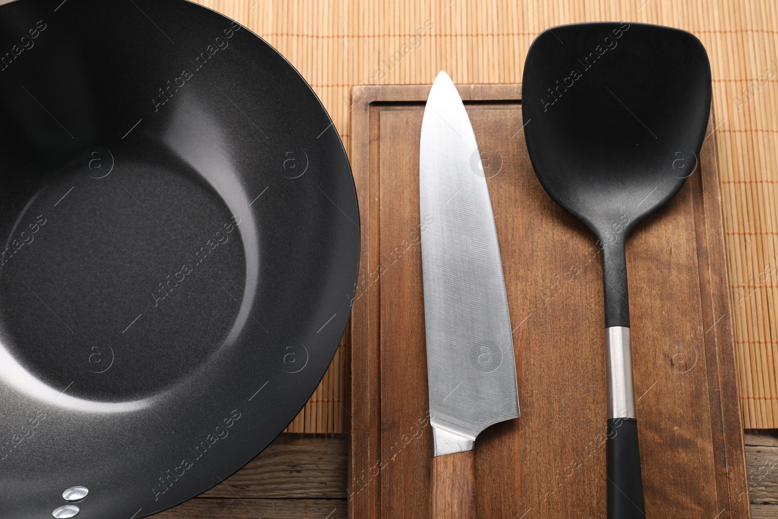 Photo of Black metal wok, knife and spatula on wooden table, top view