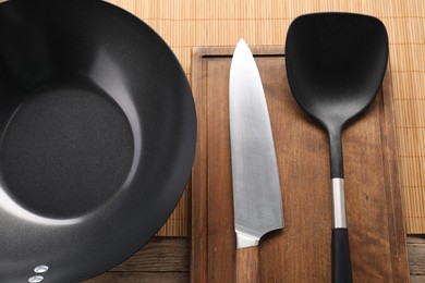 Photo of Black metal wok, knife and spatula on wooden table, top view