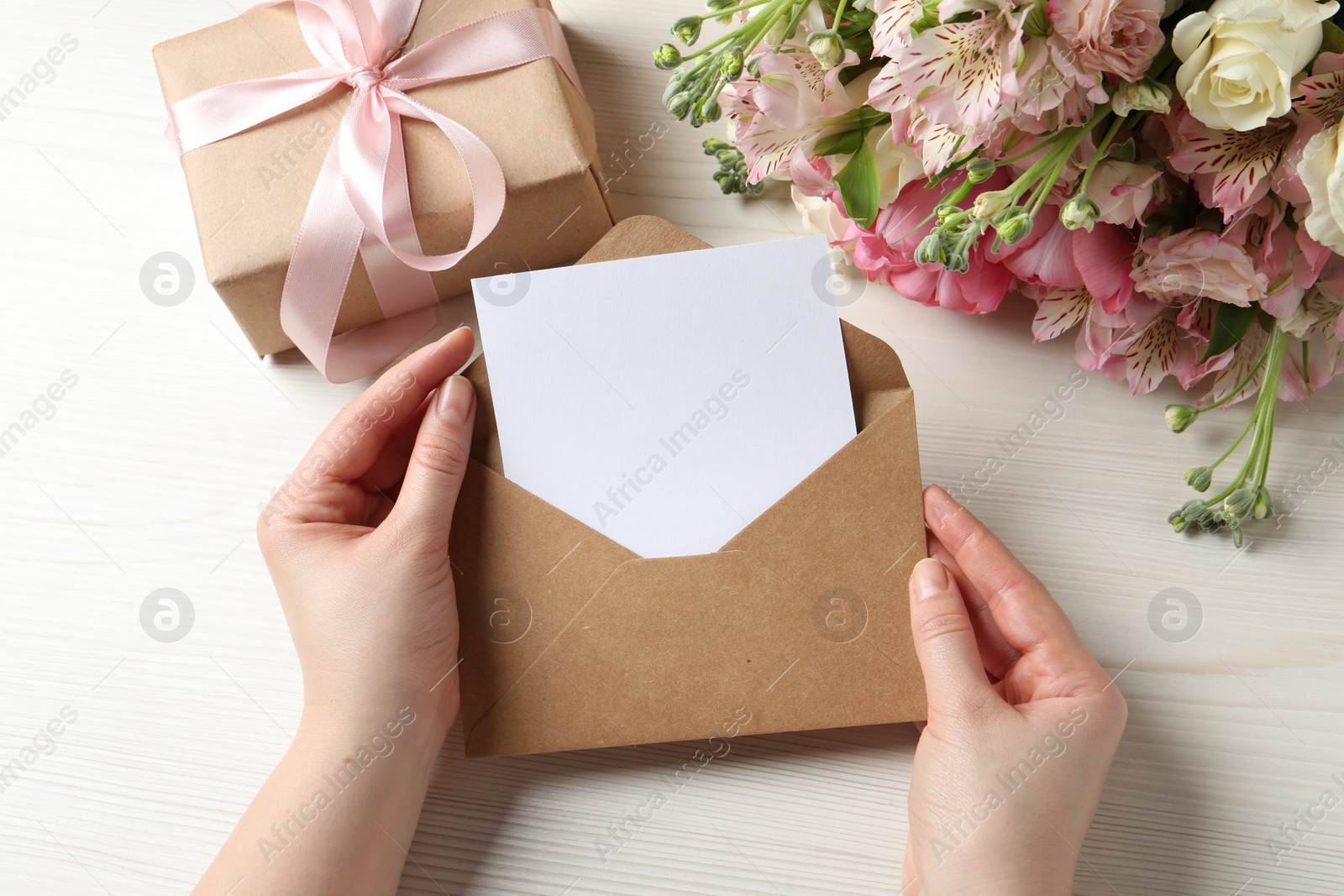 Photo of Happy Mother's Day. Woman holding envelope with blank card at white wooden table, top view