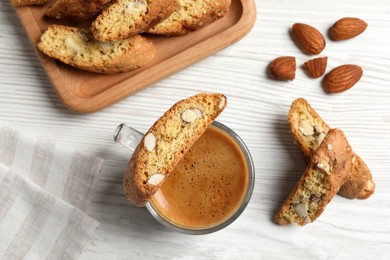 Photo of Tasty cantucci, cup of aromatic coffee and nuts on white wooden table, flat lay. Traditional Italian almond biscuits
