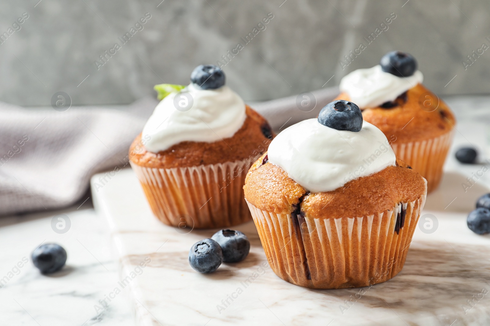 Photo of Marble board with tasty muffins, cream and blueberries on table