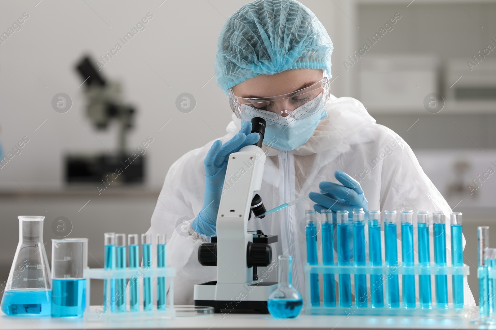 Photo of Scientist dripping sample onto Petri dish while working with microscope in laboratory.