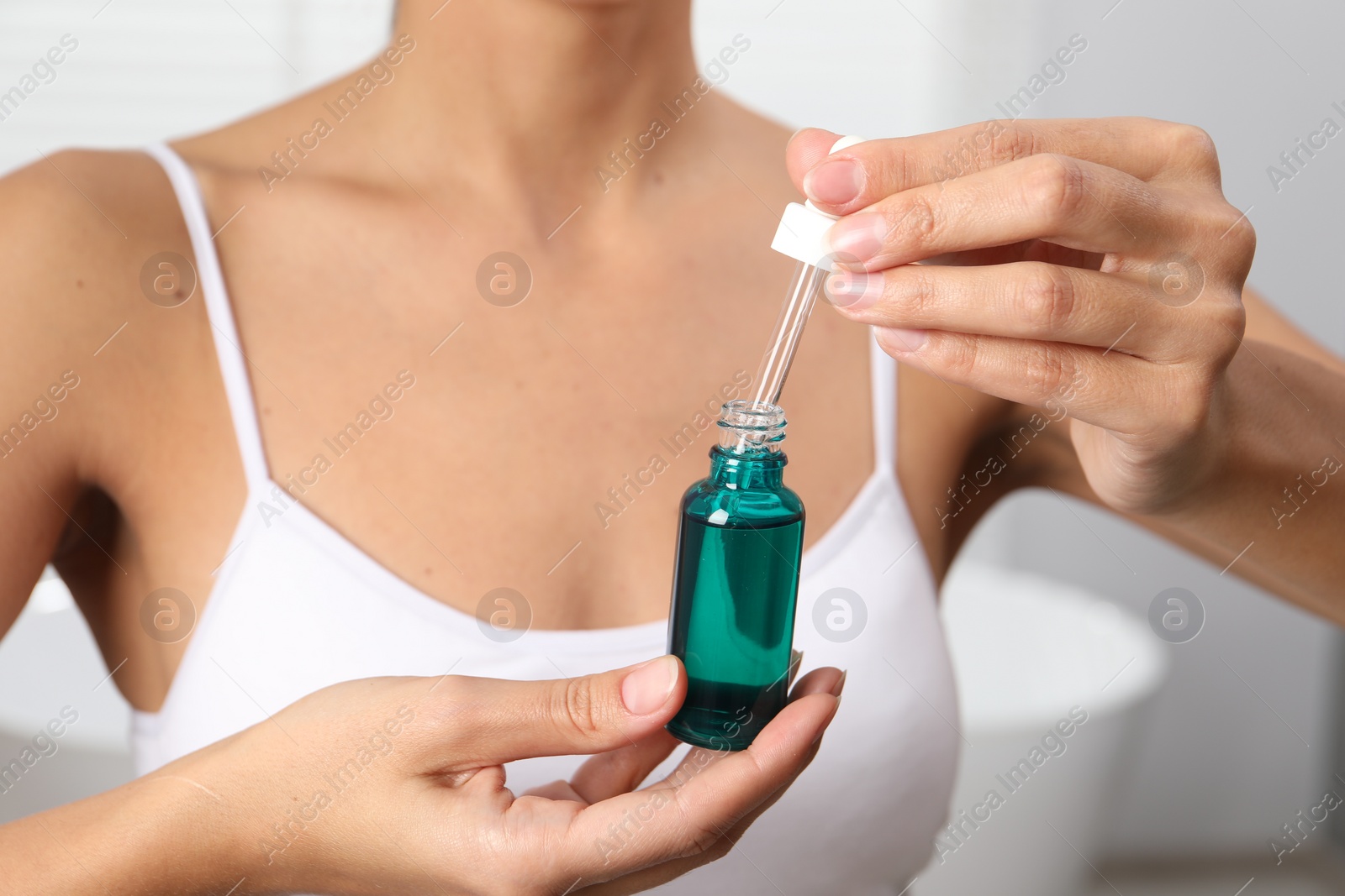 Photo of Woman with bottle of cosmetic serum on blurred background, closeup