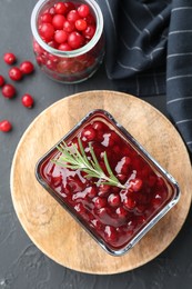 Photo of Tasty cranberry sauce in bowl and glass jar with fresh berries on gray textured table, flat lay