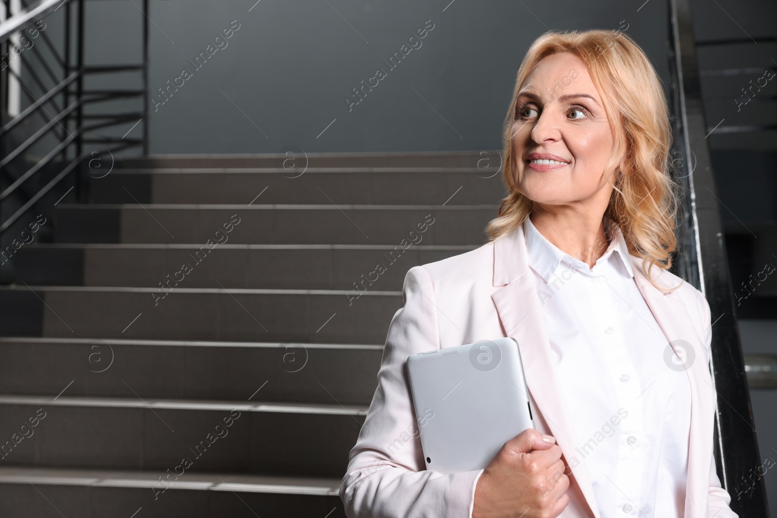 Photo of Happy lady boss with tablet near staircase indoors, space for text. Successful businesswoman