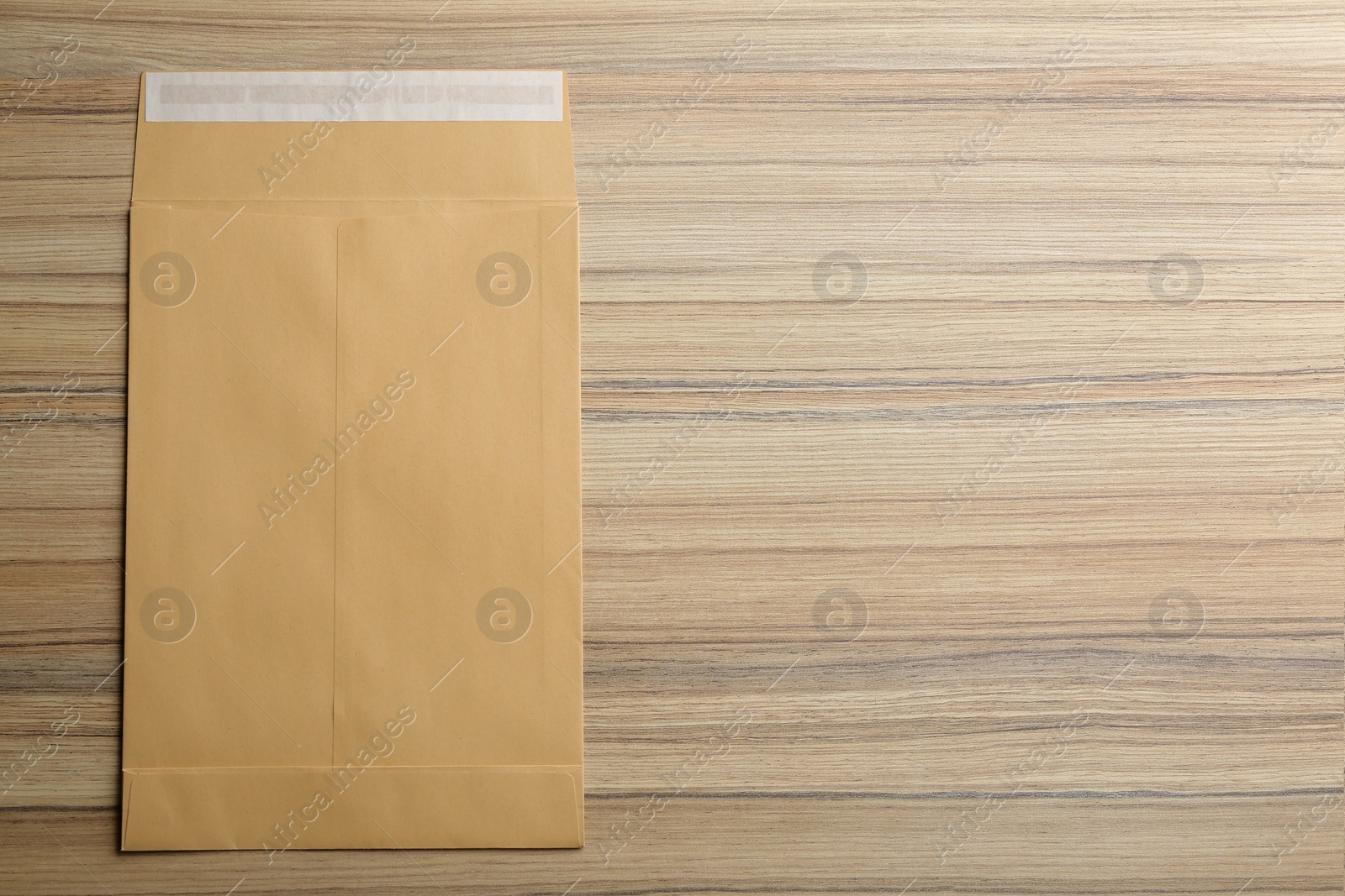 Photo of Kraft paper envelope on wooden background, top view. Space for text
